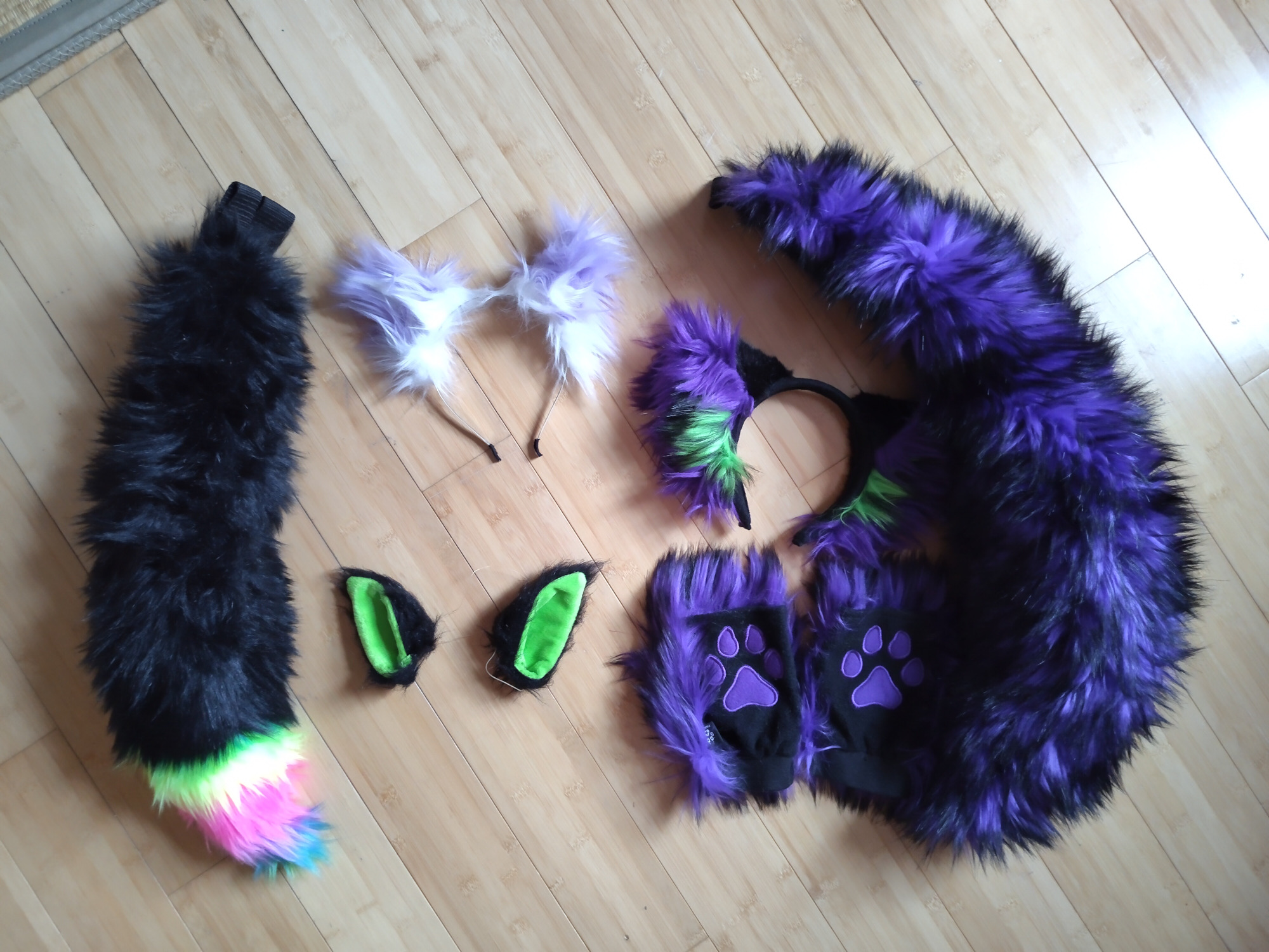 Fur partials I have gathered over the years. Only a few pieces but they are each very special to me. Clockwise, large purple and black fox tail, matching purple, black ,and green ears, then some black with green interior elastic band mounted ears, a samller tail on far left, mostly black with a smattering of colors at tail tip, and last at top a pair of headband mounted lavender and white ears